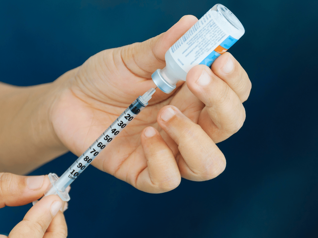 A person drawing insulin from a small vial into a needle.